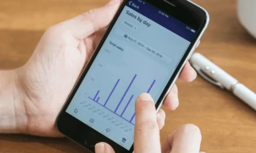 Person analyzing daily sales graph on smartphone screen.