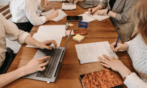 A collaborative workspace with multiple people brainstorming, writing notes, and using a laptop on a wooden table.