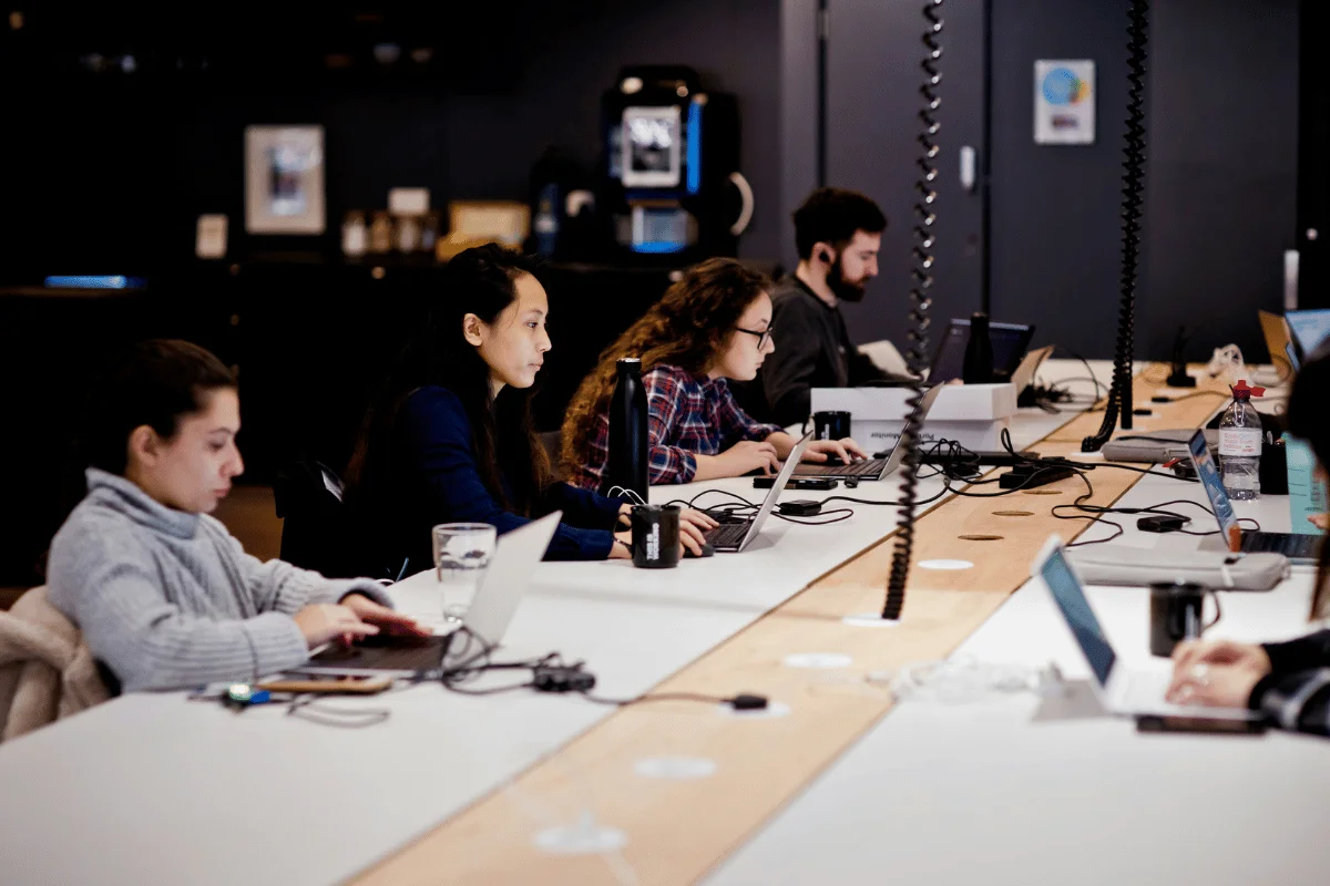 People working on laptops at a shared office desk.