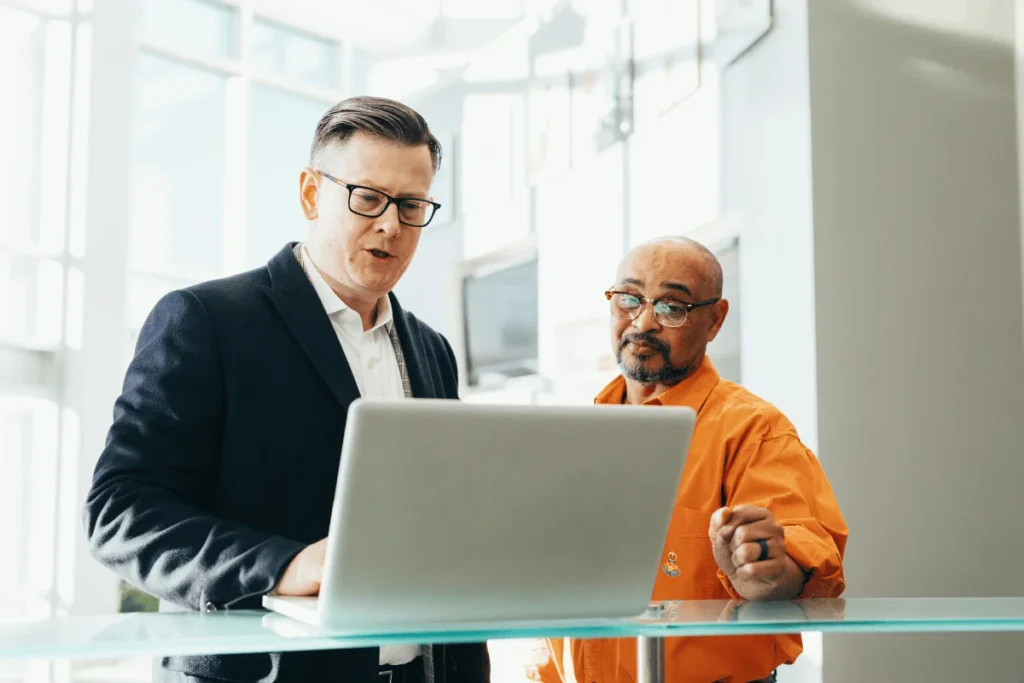 Two businessmen reviewing data on a laptop in a bright office.