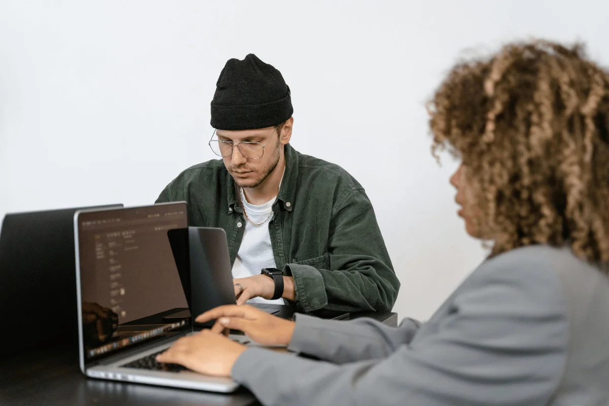 Best Practices for Using Dynamics 365 Customer Engagement Effectively Two individuals work on laptops at a table, focused on their screens in a modern, minimalist office setting.