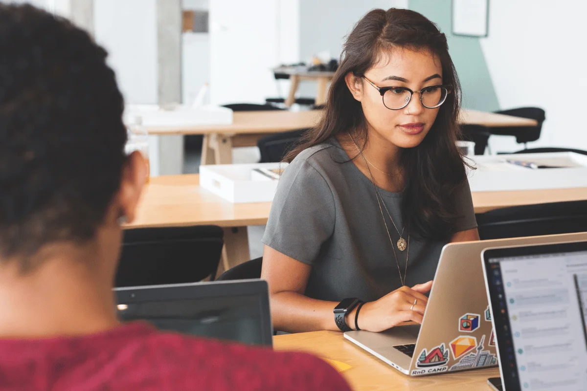 Woman in glasses working on laptop with stickers in office.