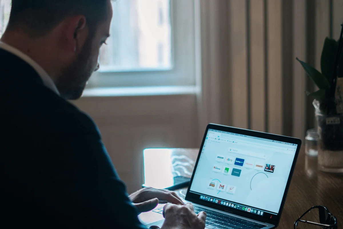 Challenges in Implementing MS Dynamics 365 Customer Engagement An individual sitting at a wooden table using a laptop displaying various website icons, with natural light filtering through a window.