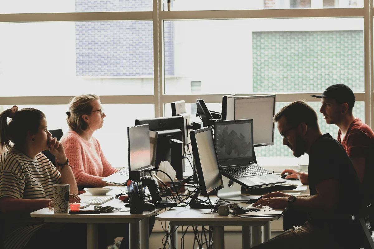 Group of people working at desks with multiple monitors.