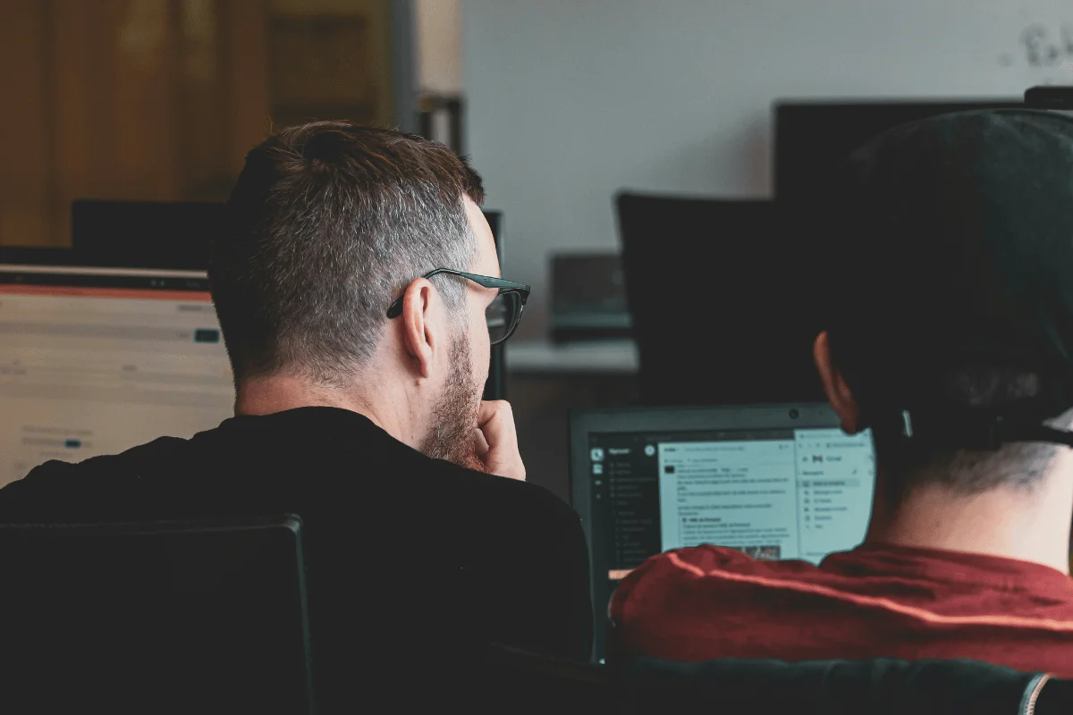 Two men working closely together on laptops in an office setting.