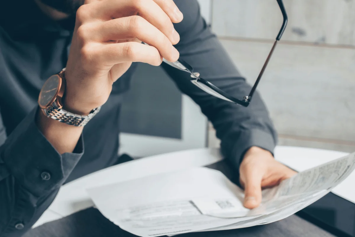 Businessman holding eyeglasses while reviewing financial paperwork.