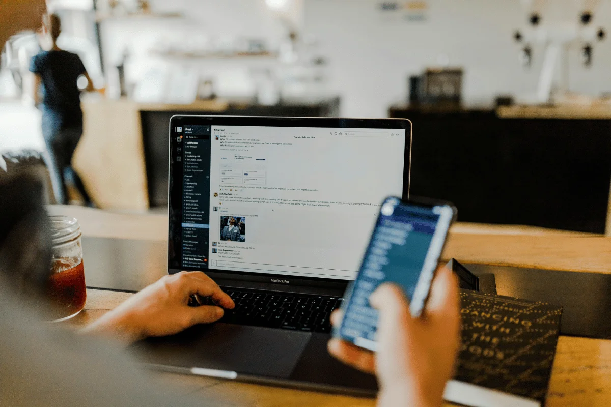 Person working on a laptop while holding a smartphone.