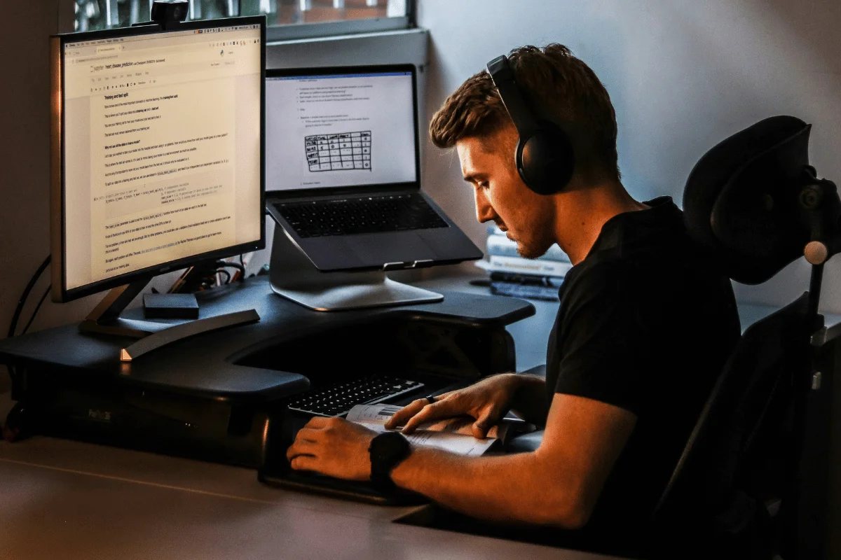 Focused man wearing headphones working on dual monitors at desk.