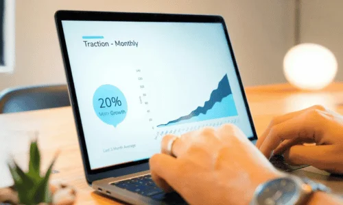 A person typing on a laptop showing a graph with a 20% monthly growth label and a "Traction - Monthly" header.