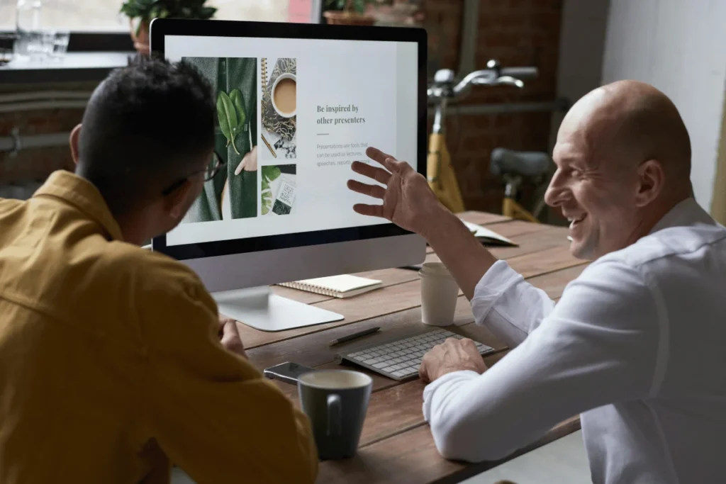 Two men reviewing a presentation on a desktop in a casual workspace.