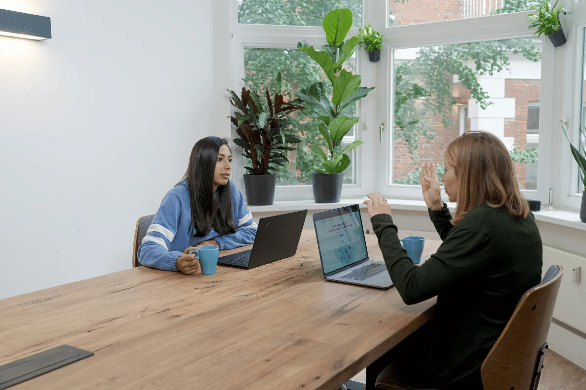 Two women having a business discussion with laptops at a wooden table.