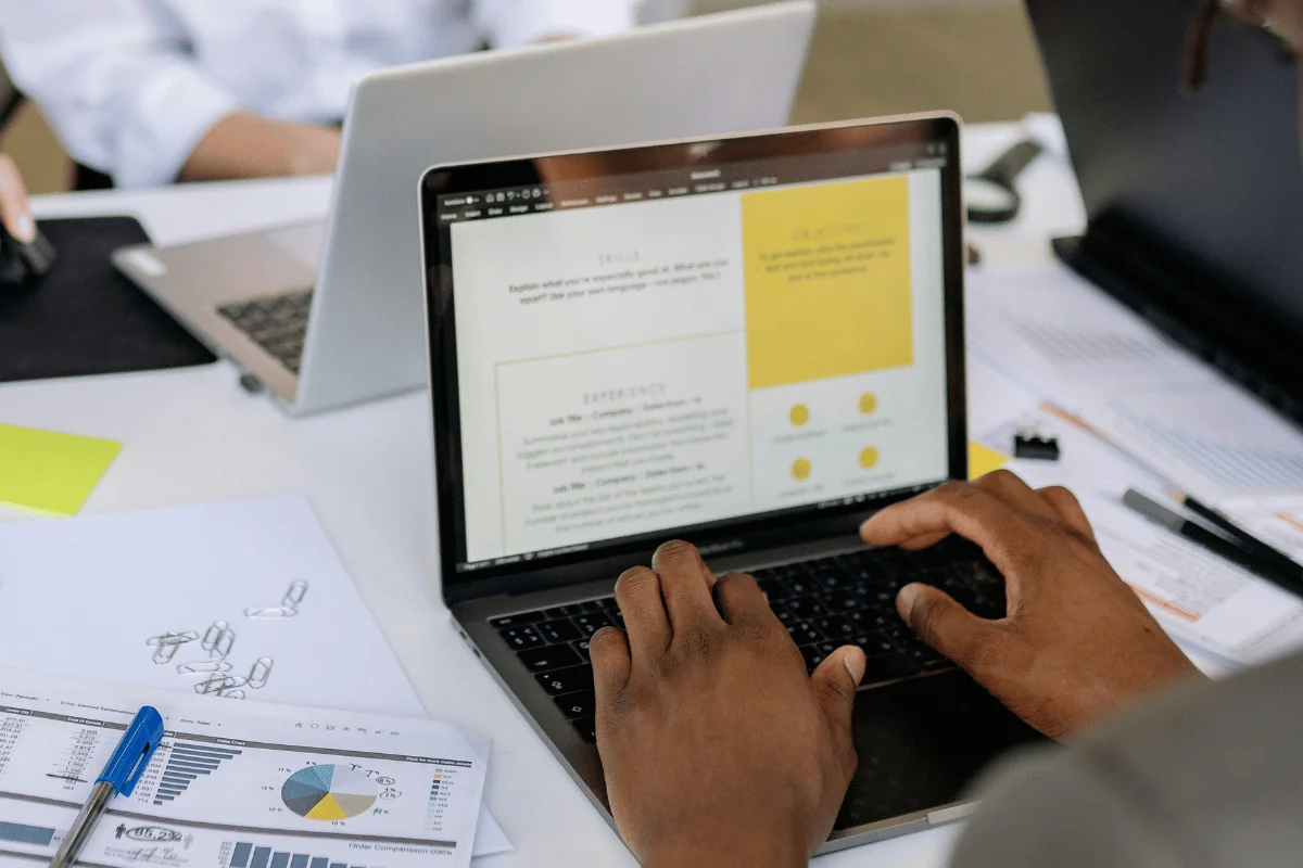 Person working on a resume or document on a laptop at a desk.