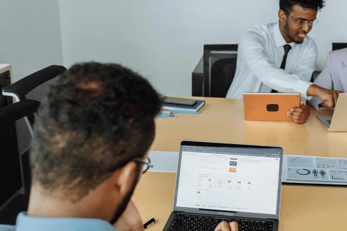 What Is Dynamics 365 Customer Engagement A group of professionals collaborates in a meeting, using laptops and tablets on a conference table. Graphs and data sheets are visible.