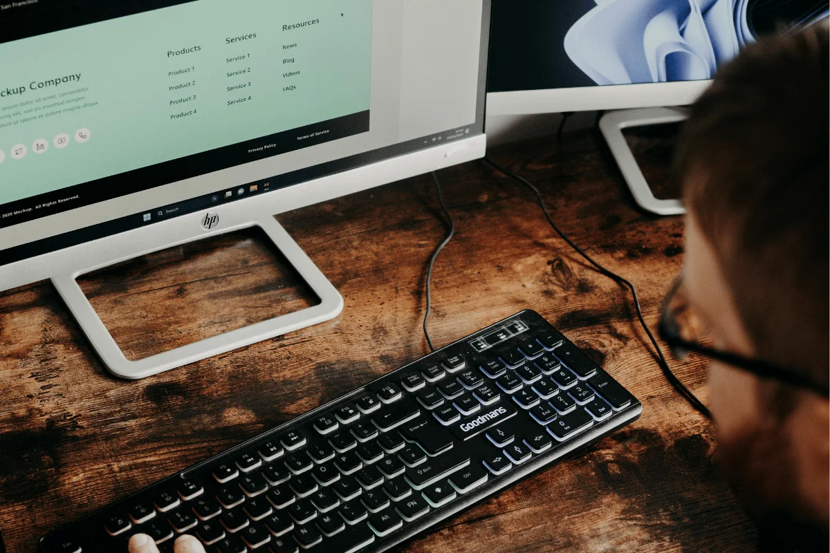 Man working at desktop computer with dual monitors in office.