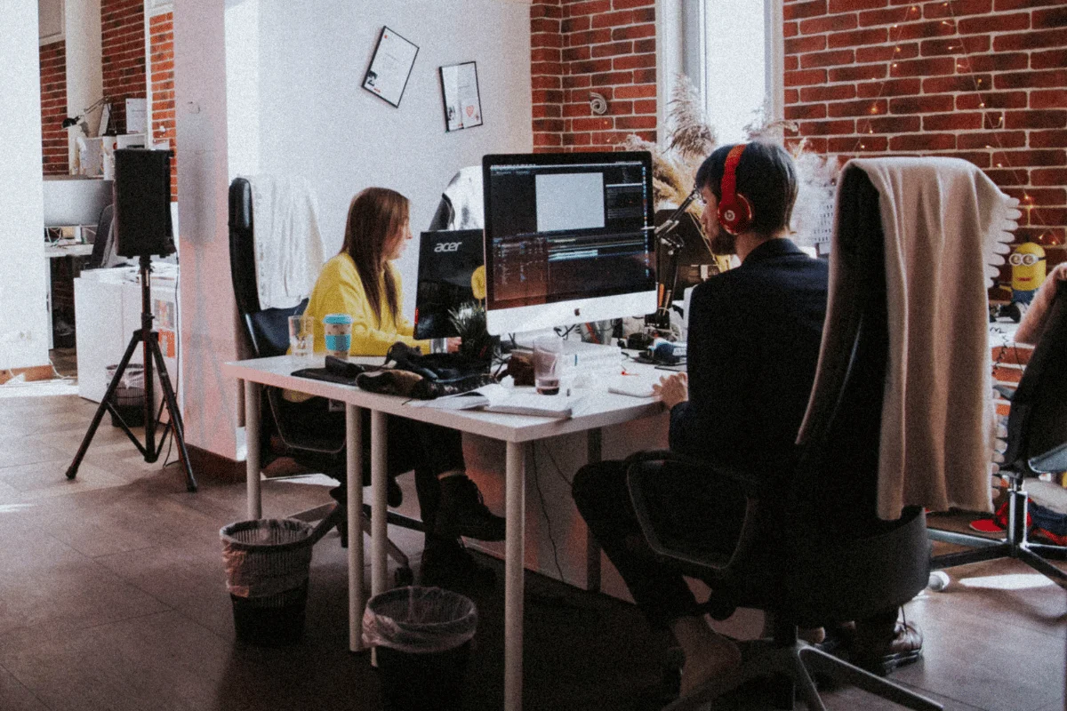 Two coworkers working on desktop computers in creative office space.