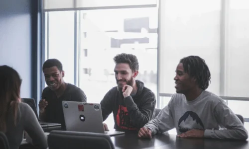 Hand holding phone while working on laptop with Cyrillic keyboard.